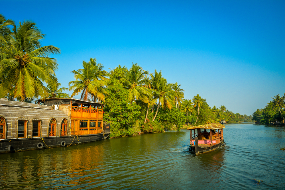 A,Tourist,Boat,Passes,Through,A,Traditional,Kerala,Houseboat,On